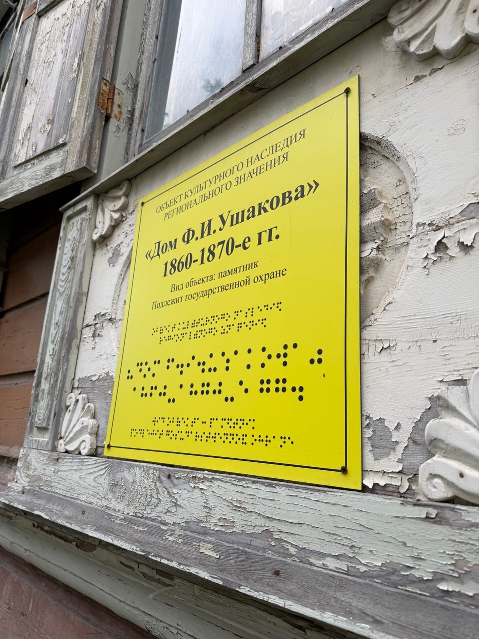 Жёлтая табличка на фасаде в Тюмени: под текстом видны строки точек, изображающих шрифт Брайля